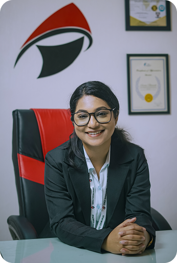 Woman in business suit sitting on black and red office chair with certificates on wall behind