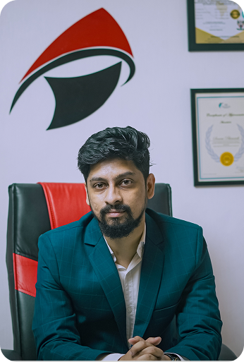 Man in business suit sitting on black and red office chair with certificates on wall behind