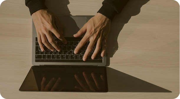 Top view of hands typing on a laptop keyboard on a wooden desk